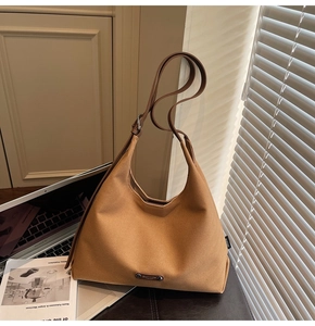 Detail of camel suede tote bag with metal emblem on brown leather surface