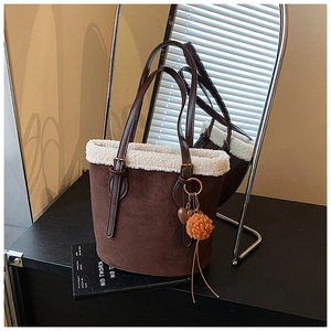 Close-up of brown suede bucket bag with white fleece trim and decorative pom-pom on book