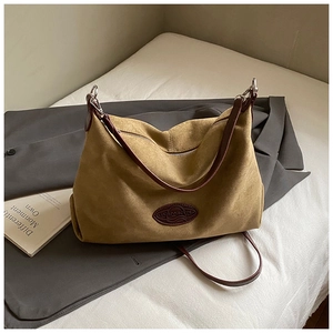 Close-up of brown suede shoulder bag showing texture and leather logo on grey blazer
