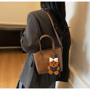 Brown leather bucket bag detail with a cute plush bear charm and golden metal hardware