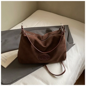 Detailed view of brown suede tote bag with leather strap and silver zipper on white fabric