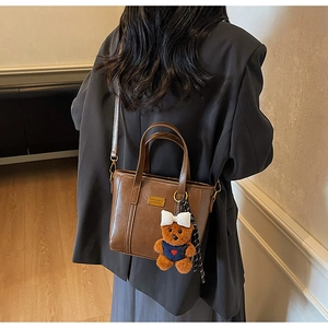 Detail of dark brown faux leather tote bag featuring a cute plush bear charm and gold plaque