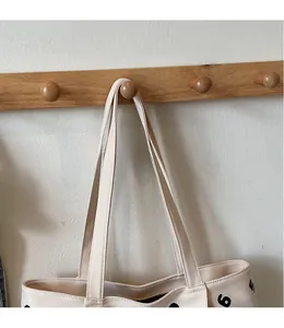 Detail of cream canvas tote bag with long shoulder straps and black numeric print on a hook