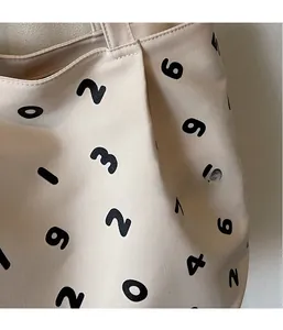 Close-up detail of beige canvas tote bag showing black numeric prints and sturdy handle