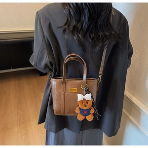 Detailed view of a brown vintage bucket bag featuring a cute teddy bear charm and gold plaque