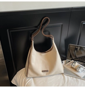 Detail of beige canvas hobo bag showing brown leather trim and metal logo plate