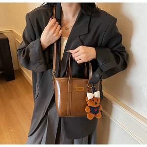 Close-up of retro brown bucket bag with golden logo plate and cute plush bear charm
