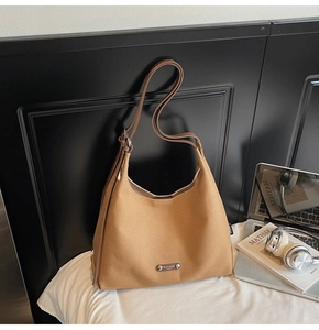 Brown leather hobo shoulder bag with adjustable strap next to a laptop and books