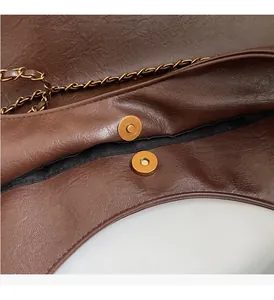 Close-up of brown textured leather bag featuring bronze magnetic buckle and chain
