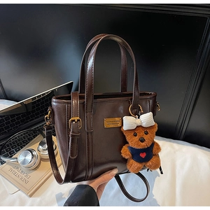 Macro shot of dark brown glossy leather tote featuring a golden plate and teddy bear charm