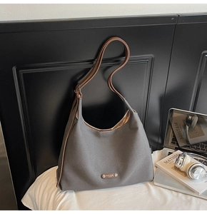 Detail of grey canvas tote bag with brown leather straps on white bed background