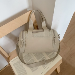 Dettaglio di una borsa a tracolla in nylon beige con cerniere multiple su sedia