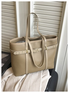 Detailed macro view of khaki lychee grain leather texture and gold hardware on tote bag