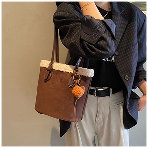Close-up of brown suede tote bag with plush white faux fur trim and orange pom-pom detail