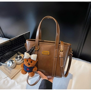 Detail view of a vintage brown leather bucket bag with a cute plush bear pendant accessory