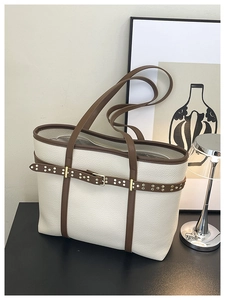 Detailed view of cream tote bag with lychee texture, brown leather trim, and gold studs