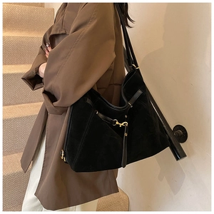 Detail view of black faux suede tote bag with gold hardware worn by model on shoulder