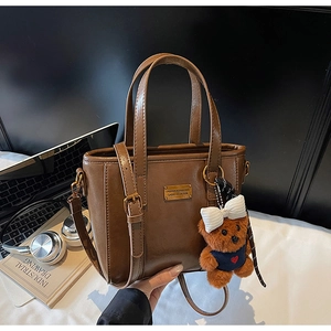Detail of dark brown vintage bucket bag featuring a cute teddy bear charm and gold hardware