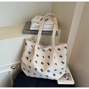 Detailed close-up of a cream canvas tote bag with black numeric print on a wooden stool