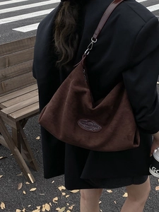 Large dark brown suede hobo bag worn by a model in a street style outdoor setting