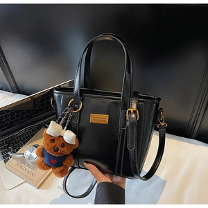 Detail of black leather tote bag with a cute bear plush charm and gold hardware