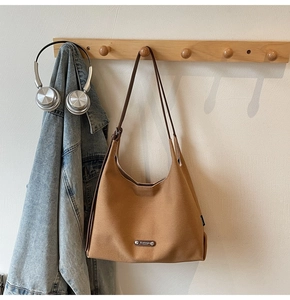 Brown canvas hobo bag on a wooden hook featuring premium leather straps and metal details
