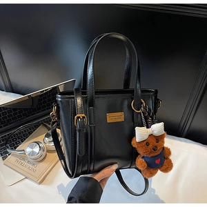 Detail view of black glossy tote bag with golden plaque and a cute brown plush bear charm