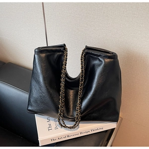 Detail view of a large black tote bag with vintage gold chain strap on an art book