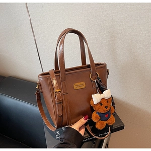 Detail of vintage dark brown tote bag with gold logo plaque and cute teddy bear charm