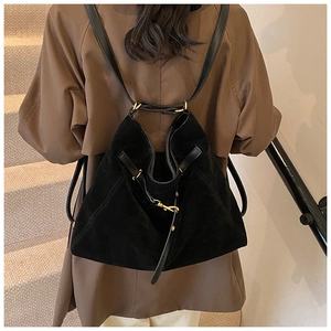 Detail of black suede backpack with gold buckles worn over a brown coat on a model