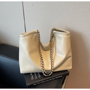 Detail of a beige tote bag with gold chain strap placed on a stack of books