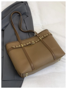 Detail of brown lychee texture tote bag with gold metal buckle and rivet belt design