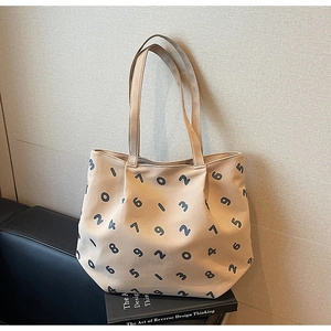 Detail view of beige canvas tote bag with black numeric print on a leather sofa