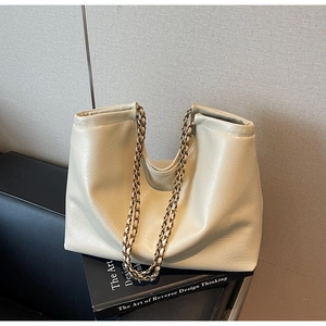 Detail of soft cream leather tote bag featuring golden chain straps and natural texture