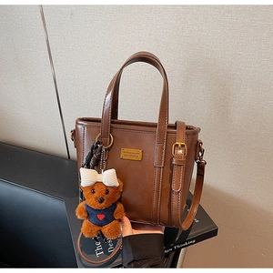 Detail of dark brown faux leather tote with golden plaque and teddy bear charm