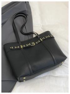 Detail view of black lychee grain leather tote bag with gold rivets and buckle