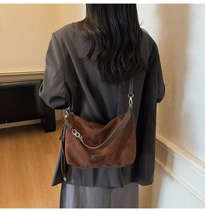 Detail of dark brown suede crossbody bag with metallic chain and brand logo plaque