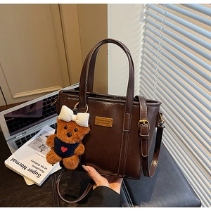 Detailed close-up of dark brown bucket bag with gold logo and cute bear charm accessory