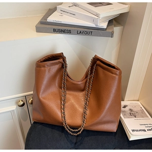 Detail of caramel brown leather tote bag with gold chain strap and brand embossing