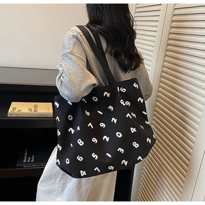 Detail of black canvas tote bag with white numeric print worn by a person in a minimalist room