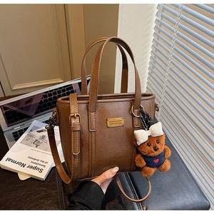 Detail of a brown leather bucket bag featuring a gold nameplate and a plush bear charm