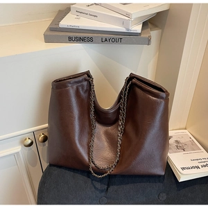 Detail of dark brown leather tote bag with chain strap on blue corduroy surface