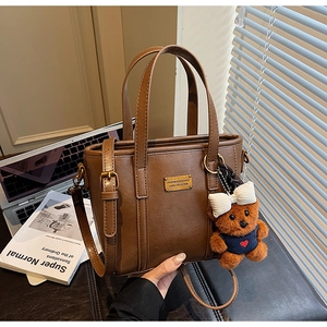 Detail of brown leather bucket bag with gold metal plate and plush bear charm
