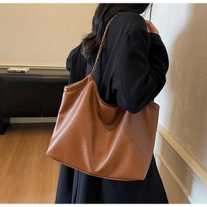 Model wearing a large brown retro tote bag with chain strap and pebble leather texture