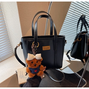 Detail of black glossy PU tote bag with gold metal plate and cute brown plush bear charm