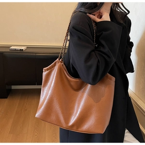 Detailed view of brown leather tote bag with chain strap worn by a model in warm light