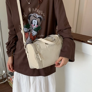 Dettaglio della borsa a cilindro in nylon color crema indossata da una persona