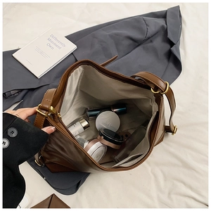 Detailed view of large dark brown suede tote bag interior with cosmetics on bed