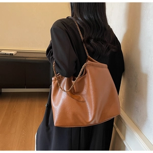 Brown faux leather tote bag with metal chain strap worn by model in a minimalist setting