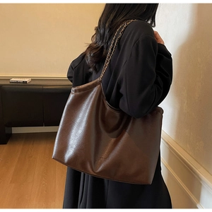 Detail of vintage brown PU leather tote bag featuring elegant chain woven shoulder strap